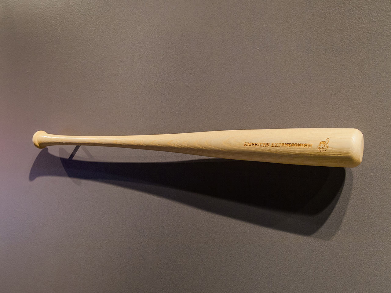 American Expansionism, 2012. An editioned baseball bat sculpture etched with the racist caricature Cleveland Indians logo and the words American Expansionism.
