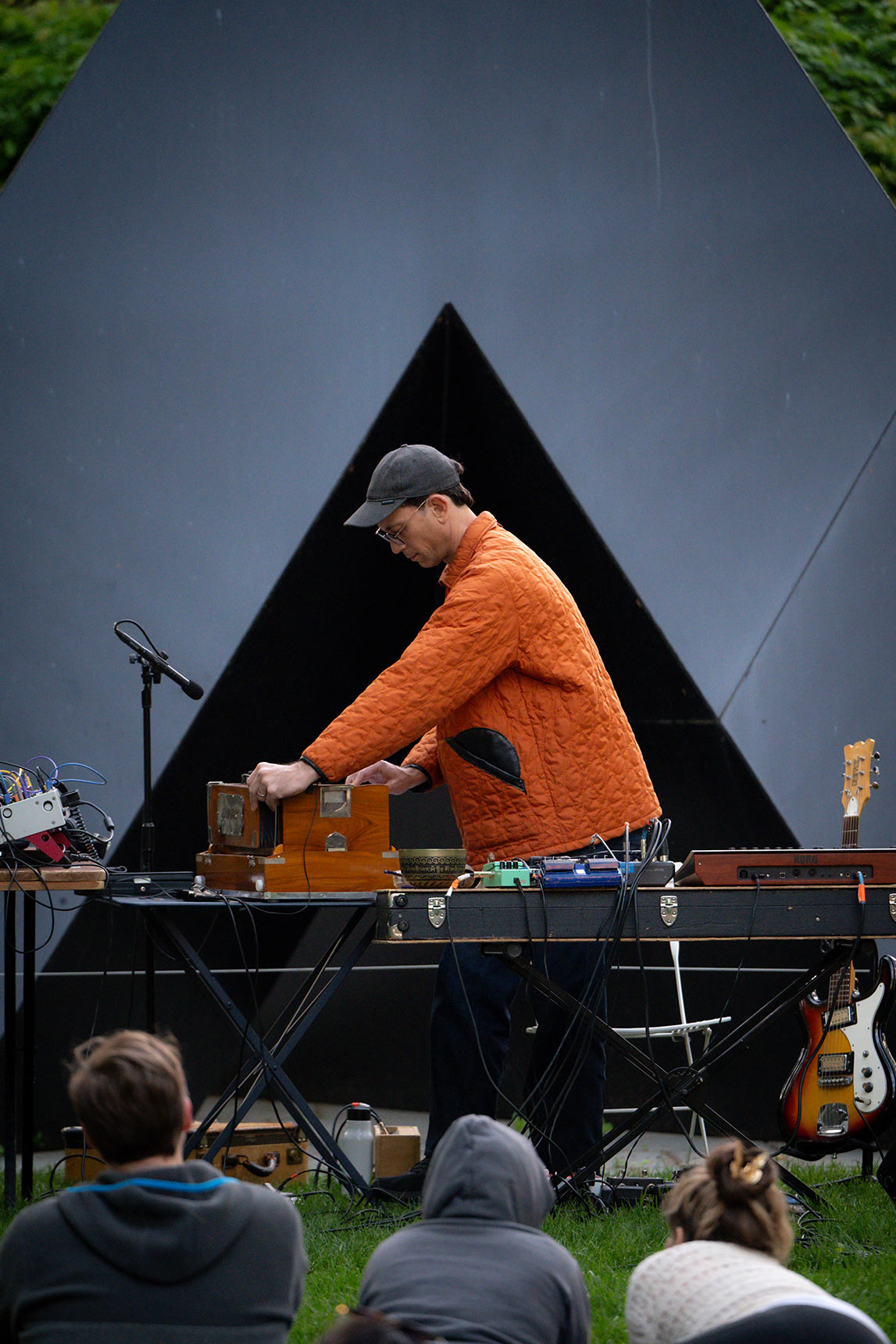 Bruce Willen playing harmonium in the BMA Sculpture Garden in front of a black triangular Tony Smith sculpture