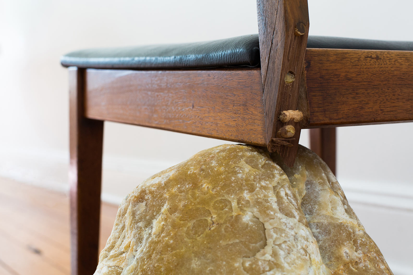 Detail of broken chair propped on a rock. Codependent Chair sculpture