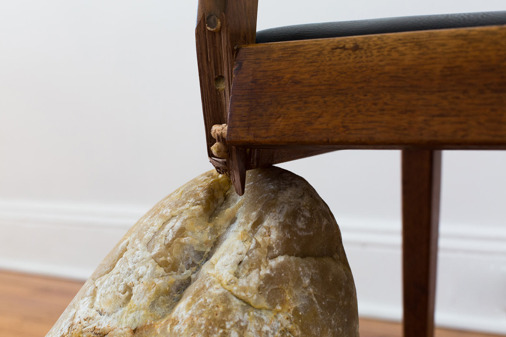 Detail of broken chair propped on a rock. Codependent Chair sculpture